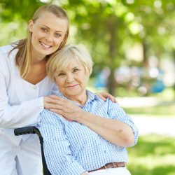 Pretty nurse and senior patient in a wheelchair looking at camera outside